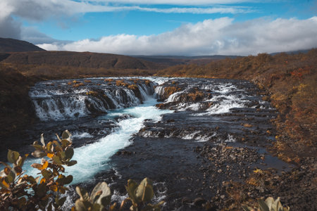 Bruarfoss waterfall in Iceland, known for its vivid blue water and dark lava rock, flows through autumn-colored terrain under a crisp sky. A hidden gem of natural beauty. Golden circle, Iceland.の写真素材