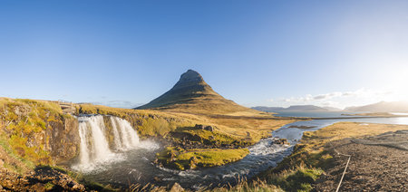 Kirkjufell mountain at sunrise with golden grasslands and soft clouds above, creating a peaceful and iconic Icelandic scene on the Snaefellsnes Peninsula.の写真素材