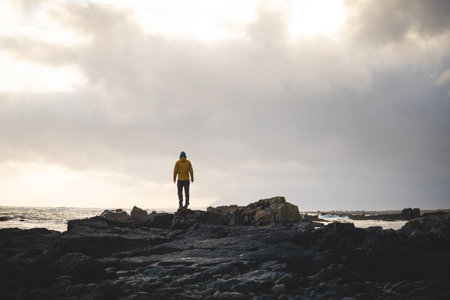 Young traveler walks along a rocky beach during a breathtaking stormy sunset in western Iceland, enjoying the last rays of sunlight. Dramatic sky and soft Arctic light.の写真素材