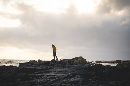 Young traveler walks along a rocky beach during a breathtaking stormy sunset in western Iceland,...