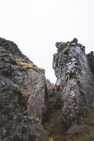 Hiker in a yellow jacket explores a dramatic lava rock passage in Iceland, surrounded by towering cliffs and mossy textures. A striking scene of natural wonder and adventure.の写真素材