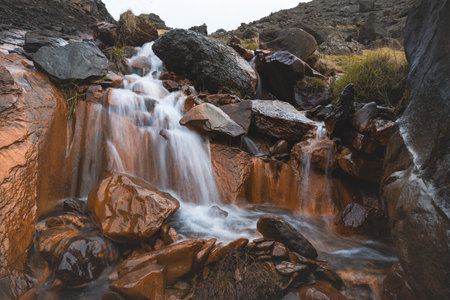 Rust-colored waterfall flows through volcanic rocks in Iceland's wild highlandsâwhere fire meets water in a surreal, untouched natural symphony.の写真素材
