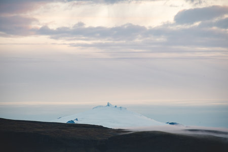 Glacier capped peak of Snaefellsjokull volcano emerges through soft morning mist in western Iceland, evoking a mystical and timeless Arctic atmosphere.の写真素材