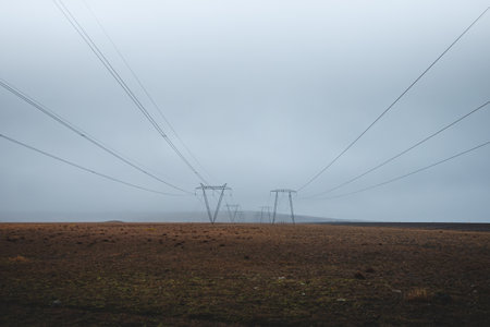 Power lines stretch endlessly across the misty Icelandic plains, disappearing into the fog. A moody, minimalist landscape capturing isolation and human presence in the wild.の写真素材