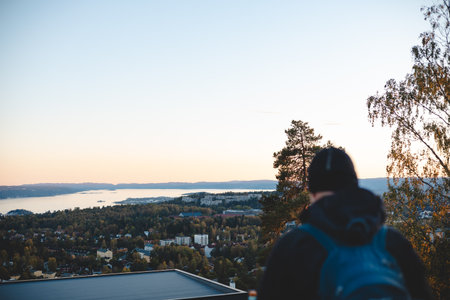 Overlooking Oslo from above, a traveler watches the sunset paint the horizon in peach and blue, embracing a serene Scandinavian evening from the heights.の写真素材