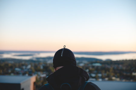 Overlooking Oslo from above, a traveler watches the sunset paint the horizon in peach and blue, embracing a serene Scandinavian evening from the heights.の写真素材
