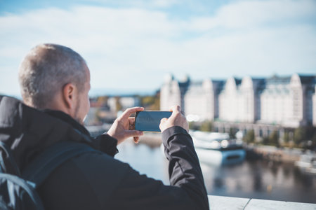 Capturing Oslo from the Opera house, a traveler frames the city through his phone. Old man is using modern technology. Taking a picture.の写真素材