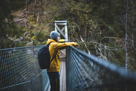 Thoughtful hiker pauses on a suspension bridge deep in Oslo Marka, wrapped in autumn quiet and forest air, blending stillness with scenic exploration. Enjoying the view.の写真素材