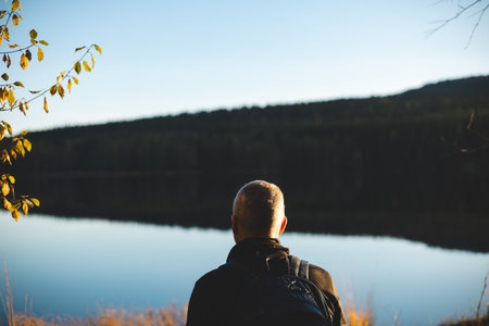 50 years old backpacker watch lake in Oslo Marka, where calm reflections and golden light embrace the silence of Scandinavian wilderness during sunset.の写真素材