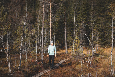 Adventurer walks on a narrow wooden trail in Oslo Marka, surrounded by golden autumn light and the silent whisper of Nordic wilderness. Norwegian raw nature.の写真素材
