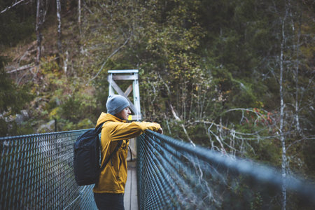 Thoughtful hiker pauses on a suspension bridge deep in Oslo Marka, wrapped in autumn quiet and forest air, blending stillness with scenic exploration. Enjoying the view.の写真素材