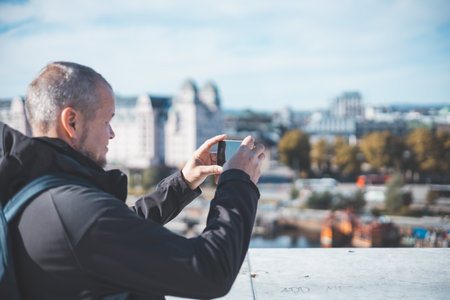 Capturing Oslo from the Opera house, a traveler frames the city through his phone. Old man is using modern technology. Taking a picture.の写真素材