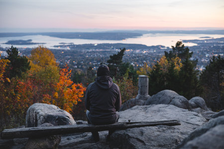 Old traveler sits on bench overlooking Oslo slowly falling asleep under the setting sun, as everything turns orange and pink. View from Vettakolltoppen, Norwegian nature.の写真素材