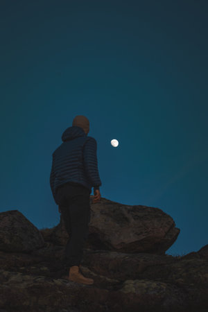 Silhouette of a man standing on rocks beneath the moon in Norway. A serene Nordic evening filled with silence, space, and the beauty of pure minimalism.の写真素材