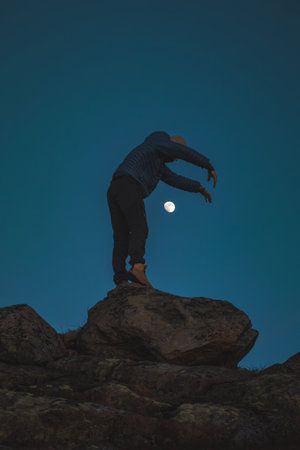 Silhouette of a man standing on rocks beneath the moon. A serene Nordic evening filled with silence, space, and the beauty of pure minimalism.の写真素材