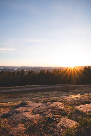 Golden rays touch treetops above Oslo as the sun sets over hills and fjords, creating a warm balance between Nordic wilderness and urban horizon. Grefsenkollen.の写真素材