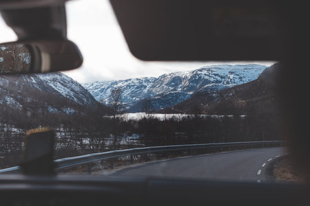View from a car driving through a snowy mountain pass in Norway. Road trip through wild landscapes and frozen valleys of the Nordic wilderness.の写真素材