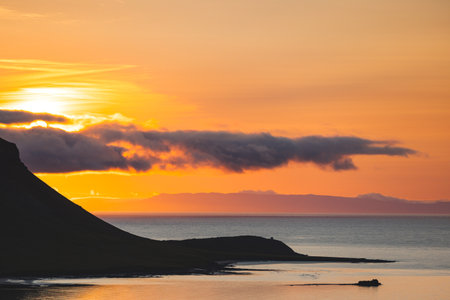 Calm sea surrounds a small island near West Iceland under warm orange summer skies, viewed from shore in a peaceful minimalist sunset panorama at sea