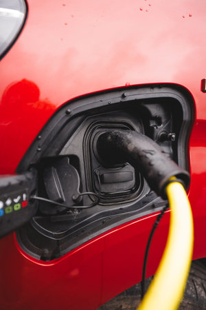Close-up of a charging plug connected to a red EV in rainy Norway in late summer, symbolizing electrification and humanityâ€™s move beyond fossil fuels