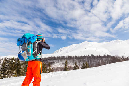 Young caucasian man photographer talking pictures while backcountry skiing on a beautiful sunny day with fresh snowの写真素材