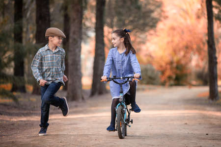 girl on a bicycle and boy running beside on the path of a parkの写真素材