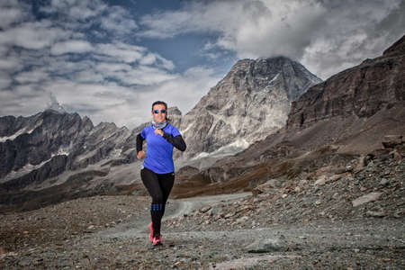 woman running down the road in the mountainous landscape of the Italian Alpsの写真素材
