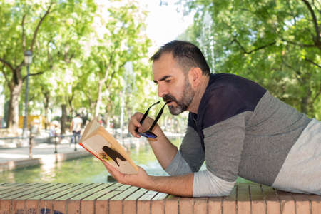 man lying in a park reading a bookの写真素材