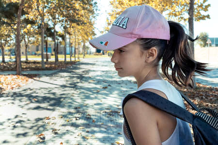 little girl with pink cap and backpack in the parkの写真素材
