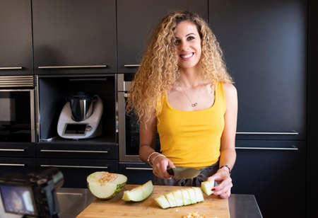 Caucasian woman cutting melon in a kitchen