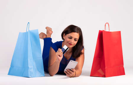 Pretty young Caucasian woman lying on the floor looking at the mobile phone and using the credit...
