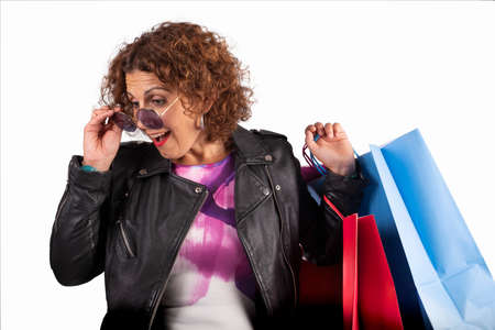 Caucasian woman with sunglasses looking down surprised, with shopping bags on white backgroundの写真素材
