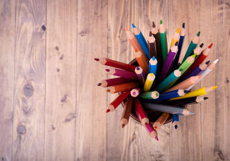 colored wooden pencils, in a brown leather beaker, seen from above, with wooden backgroundの写真素材