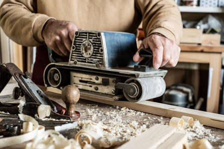 Electric belt sander, sanding machine in male hand. Processing of workpiece on light brown wooden...