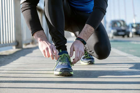 Young man tying laces of running shoes before training,closeup on shoe.