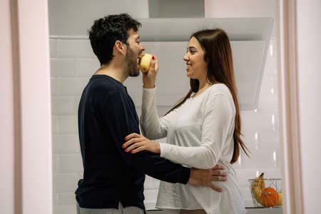 young woman giving her husband an apple in the kitchenの写真素材