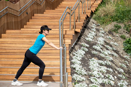 woman running in a blue t-shirt doing stretching exercises next to a wooden staircase. healthy living concept.の写真素材