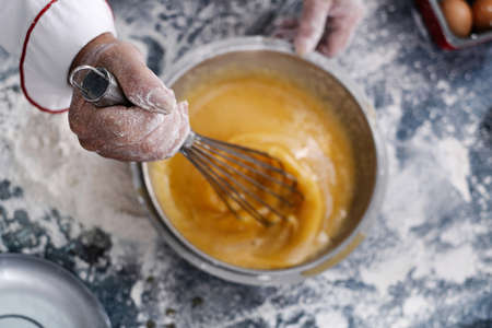 close-up of a baker's hand moving a hand blender in a muffin bowl