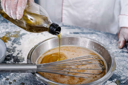 baker in a home kitchen putting oil in a steel bowl