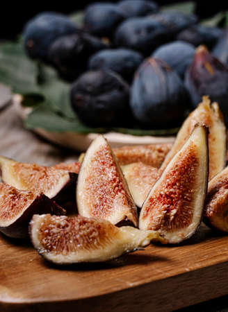 pieces of figs on a wooden board, at the bottom figs on a tray with the leaf of the fig tree