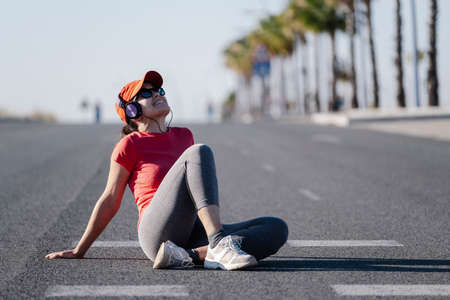 woman sitting on the road after a run with some headphonesの写真素材