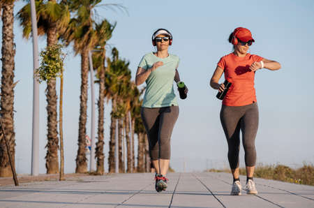 two women running along the road and listening to musicの写真素材