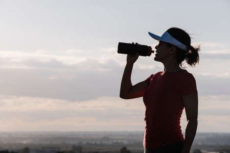 woman drinking water from a bottle against the lightの写真素材