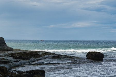 Seascape with rocks in the foreground and a boat in the backgroundの写真素材