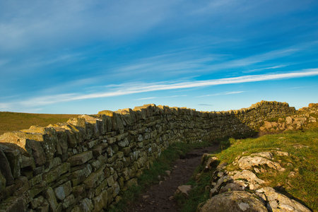 Dry stone wall leading to a path with blue sky in the backgroundの写真素材
