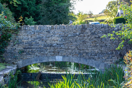 Stone bridge over a small pond in a garden on a sunny dayの写真素材