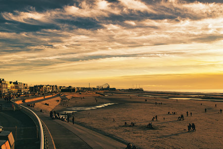 Beach at sunset with people on the sand and people walking.の写真素材