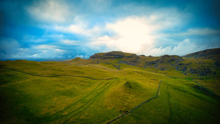 Scenic landscape with lush green fields under a dramatic sky with sunbeams piercing through clouds.