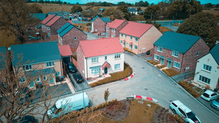 Aerial view of a suburban neighborhood with modern houses, parked cars, and a curved street. The houses have different colored roofs and are surrounded by trees and greenery.の写真素材
