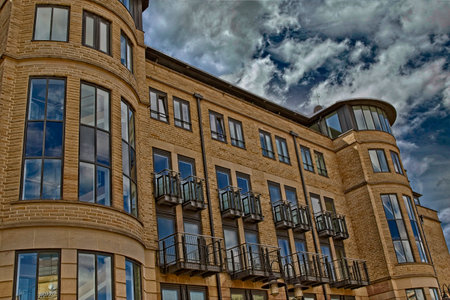 Modern multi-story building with large windows and balconies under a dramatic cloudy sky.の写真素材