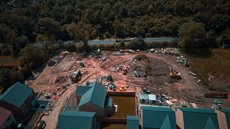 Aerial view of a construction site with houses being built, surrounded by trees and a road.